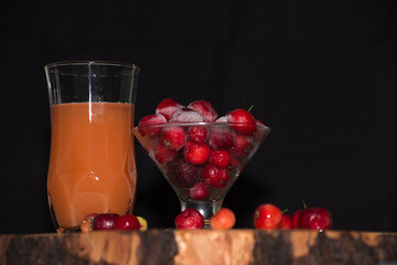 Ready acerola juice with frozen acerolas on the side. vibrant and natural colors. Rich in vitamin C, natural and healthy. rustic wooden table with black background.