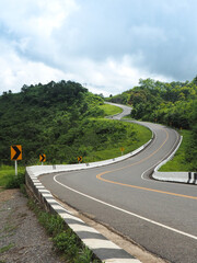 Road number three on the mountain of Nan, Thailand with yellow traffic turn notice on cloudy day.