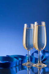 Studio photo of shiny champagne glasses with ribbons on deep blue background