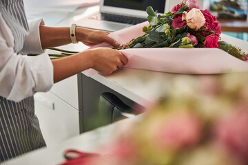 Skillful florist covering a flower composition in pink paper wrap