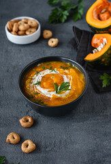 Pumpkin soup with ingredients on dark background. Vegetarian autumn pumpkin cream soup with croutons.