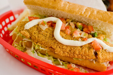 Fried fish or po boy sandwich. Classic Cajun cuisine: fried fish sandwich served on toasted bun with onions, lettuce, tomato, mayo, salt and pepper. Classic New Orleans sandwich favorite.