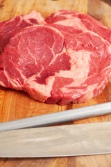 Premium rib eye steaks on a wooden cutting board with butcher sharpening steel and knife, Top quality meat product with excellent marbling which gives it special flavor.
