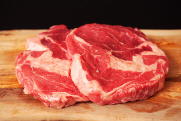 Premium rib eye steaks on a wooden cutting board, Top quality meat product with excellent marbling which gives it special flavor. Black background