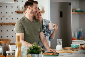 Young couple making pancakes at home. Loving couple having fun while cooking.