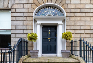 Black paneled Georgian door, with decorative lead fanlight, stone columns and granite steps at...