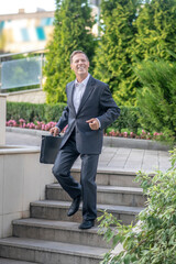 Happy mature businessman walking with case down the stairs outside