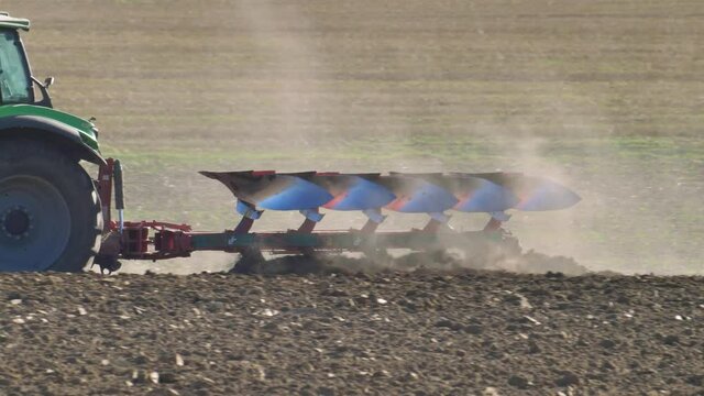 Farmer Ploughing Soil using Tractor with Mouldboard Plough on Sunny Day