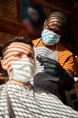 Barber in medical mask cutting client hair in barbershop