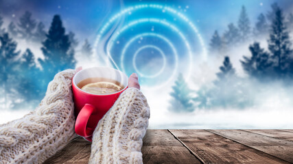 Red cup with coffee, tea in female hands on a snowy background, winter forest. A red cup in hands against the background of a winter forest landscape on soft, knitted sleeves. Coffee, tea on a wooden 