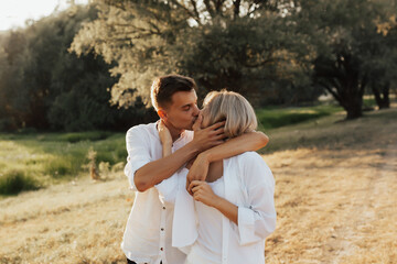 Fototapeta premium Portrait of young happy couple kissing and hugging in the summer park. They are dressed in white clothes.
