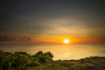 Obraz premium Seascape. Spectacular view from Uluwatu cliff in Bali. Sunset time. Golden hour. Bright sunlight on the horizon. Silhouettes of people. Nature concept. Soft focus. Slow shutter speed.