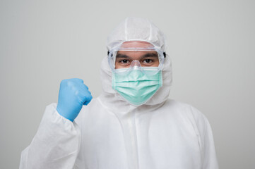 A portrait of virologist Wearing PPE suit erect his fist feel power look into camera isolated on white background. Personal Protective Equipment Concept.