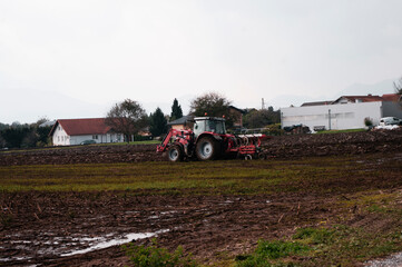 Fototapeta na wymiar Red tractor plowing field in autumn season in the village. Agriculture.