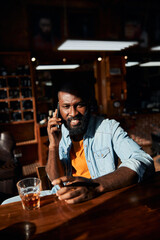 Cheerful Afro American man with cigar talking on mobile phone