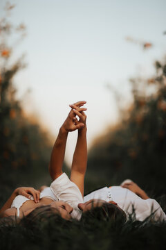 Young couple lying on grass, holding hands an looking at each other.