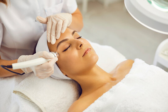 Cosmetologist making vacuum facial skin cleaning for young woman in beauty salon