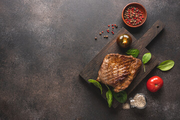 Grilled meat steak with spices on cutting board. Dark brown concrete background with empty space