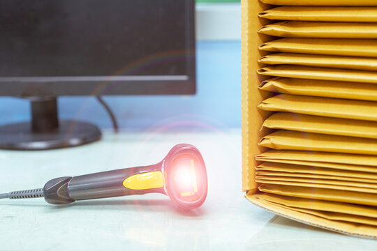 Brown paper envelopes in the box and a barcode reader on the desk wait to convert data to computer.