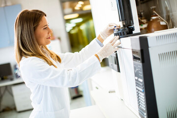 Female scientist in a white lab coat putting vial with a sample for an analysis on a gas...