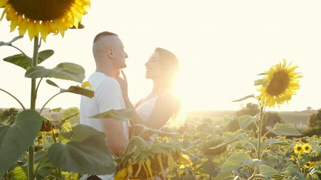 Beautiful happy couple embracing in the sunflower field. Pretty girl with her boyfriend resting outdoors. Connection with nature. Freedom concept. Happy lovers outdoors. Slow motion