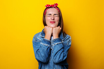 Young woman closed her eyes in a hair b.nd, in a denim jacket holds her hands under the edge on a yellow background