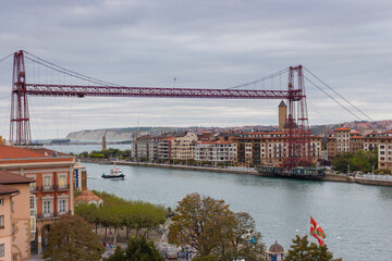 Portugalete, Spain - 10/17/2019: Biscay bridge flying with gondola and boat on river Nervion, toned. Portugalete landmark. Famous bridge called Puente de Vizcaya near Bilbao. Riverbank of Portugalete.