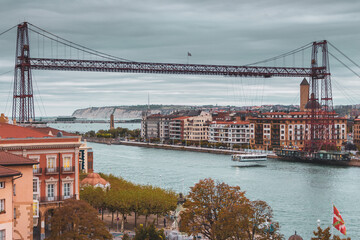 Biscay bridge flying with gondola over river Nervion, toned. Portugalete landmark. Famous bridge called Puente de Vizcaya near Bilbao. Traffic and transfer concept. Riverbank of Portugalete in autumn.