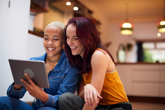 Loving Same Sex Female Couple Using Digital Tablet As They Relax At Home Together