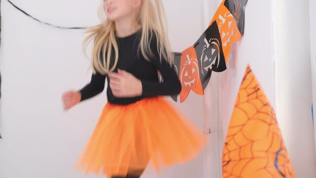 4k. Halloween Kids. Little Blonde Girl In Witch Costume Having Fun Dancing At Home, Jumping On Bed. Ready For The Holiday.