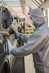 An employee of the car body paint shop with a medical mask on his face polishes the painted surface