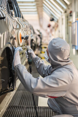 An employee of the car body paint shop with a medical mask on his face polishes the painted surface