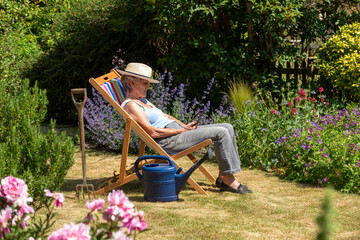England, UK. 2020. Woman taking a break from the gardening by sitting in a deckchair on a hot...