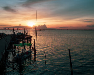 Silhouette of a fisherman boats during a beautiful orange sunset and dramatic blue sky background.