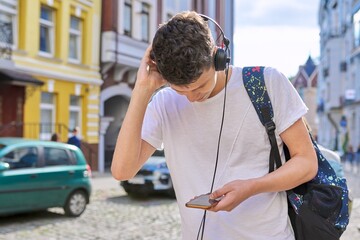 Fototapeta na wymiar Student teenager in headphones with backpack looks into the smartphone screen