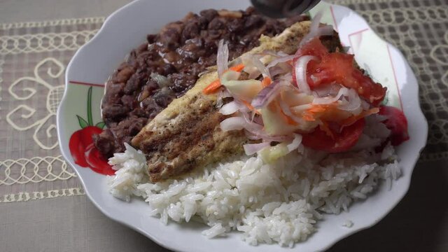 closeup tossing salad to a plate of homemade black beans with rice and fish