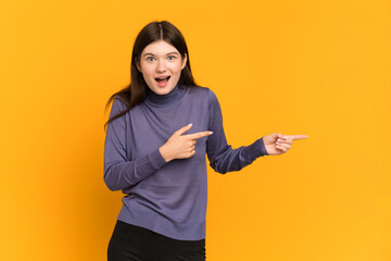 Young Ukrainian girl isolated on yellow background surprised and pointing side