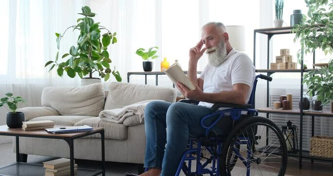 Disabled senior man in thoughts while reading a book sitting on wheelchair at home