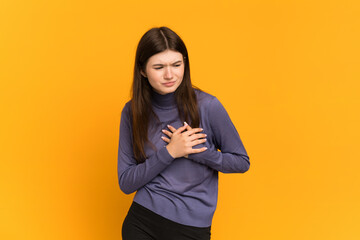 Young Ukrainian girl isolated on yellow background having a pain in the heart