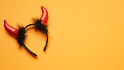 Red devil horns head hoop on orang background. Accessory for Halloween celebration, top view, flat...