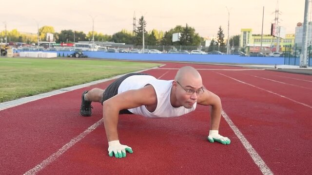 Young muscular male athlete doing exercises outdoors in the stadium
