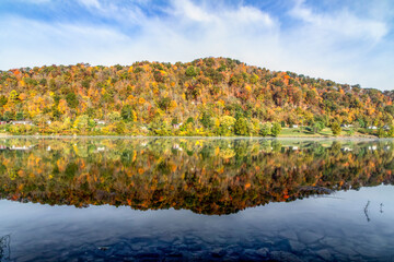 Hills with colorful fall foliage cast a beautiful reflection on the waters of the Ohio River Valley on a calm and sunny October morning as seen from the river bank at Paden City, West Virginia.