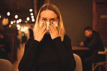 Young woman is sitting in a cafe. Blond woman in mask. Quarantine time.

