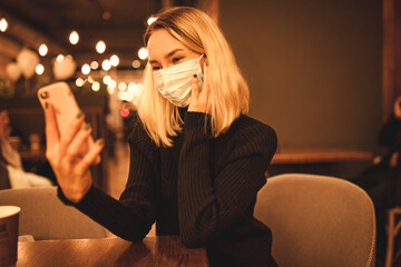 Young woman is sitting in a cafe. Blond woman in mask. Quarantine time.
