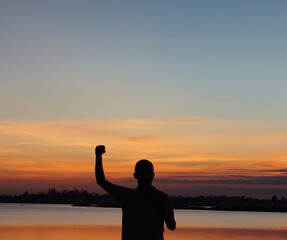 man standing by the river looking at the sunset sky. Using a silhouette technique