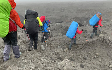 Climbers with large backpacks and trekking poles walk along the lava fields of Kamchatka.