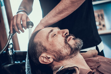 A man sits in a barbershop and washes his hair.