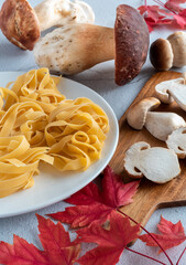 View of boletus edulis with pasta tagliatelle. There are red leaves and a cutting board