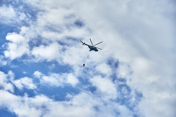 Fire fighting helicopter with water bucket on a cloudy sky background
