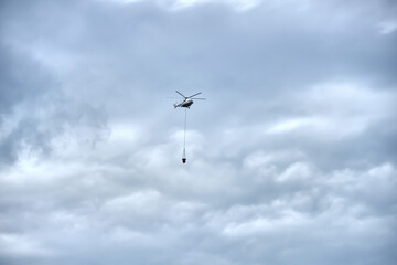 Fire fighting helicopter with water bucket on a gloomy sky background